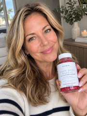 Smiling woman holding a bottle of NUTRIO Hair, Skin & Nails Multivitamin Gummies in Passion Fruit flavor
